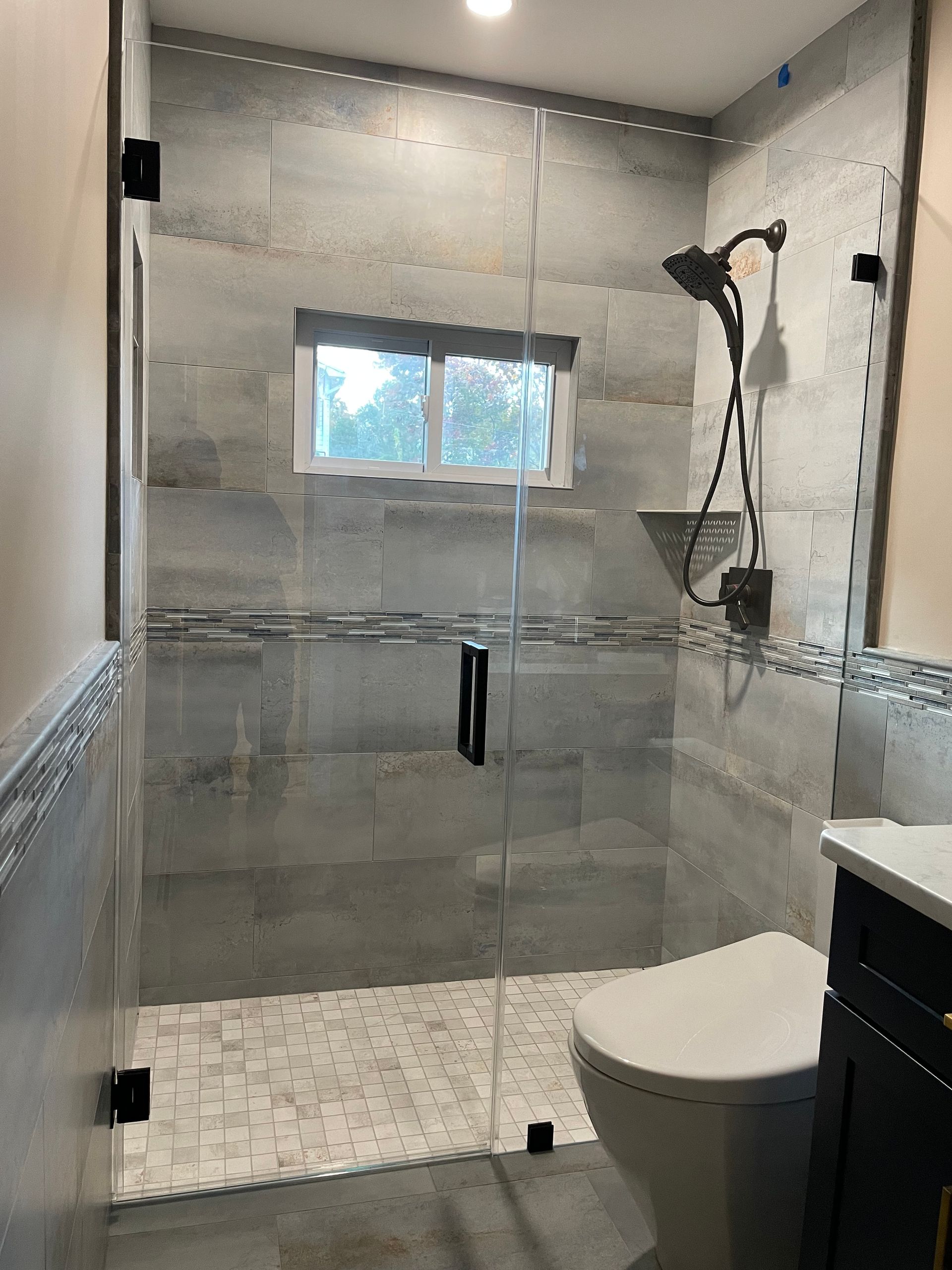 A bathroom with a walk in shower , toilet , sink and window.