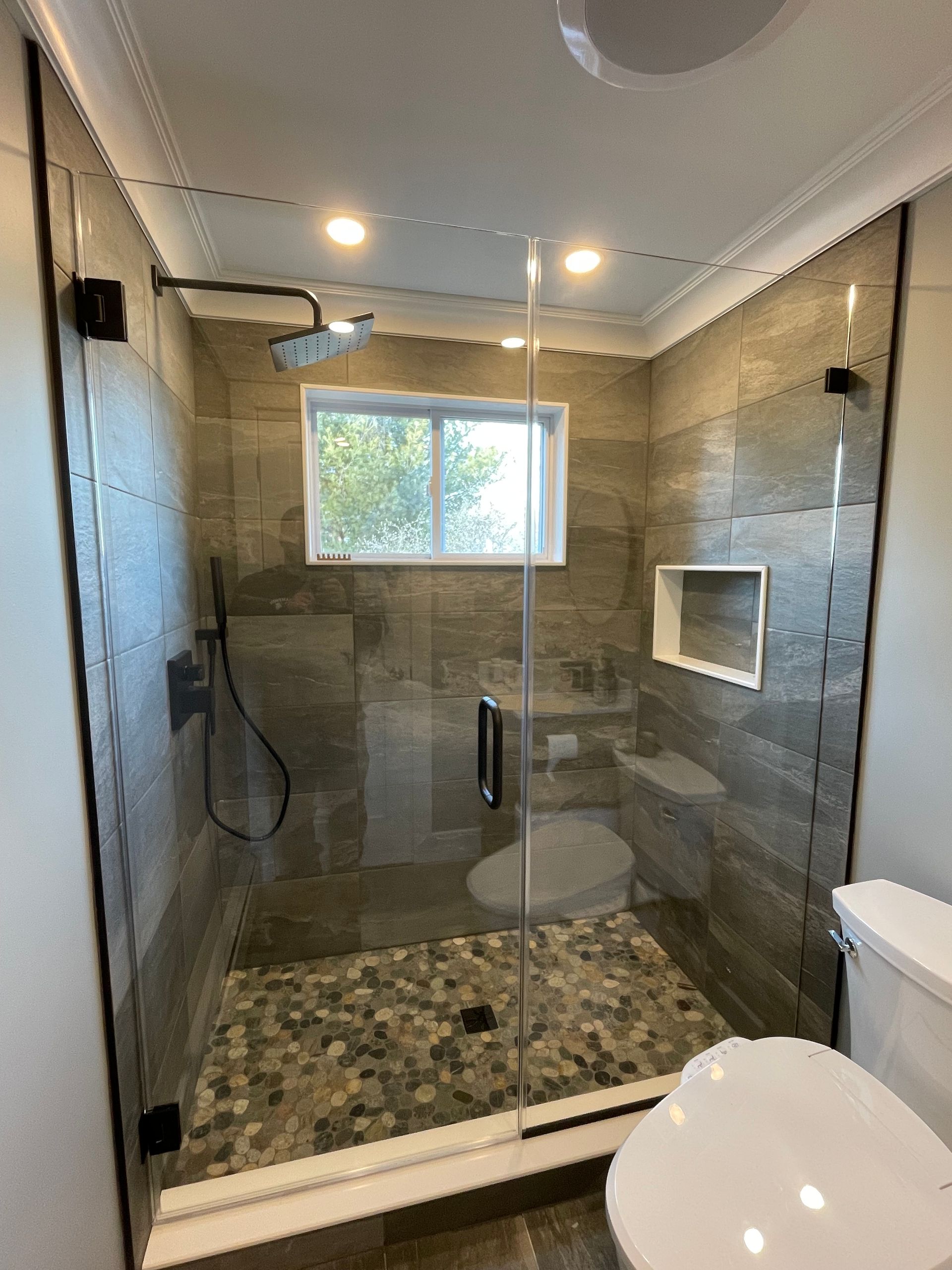 A bathroom with a walk in shower , toilet and window.
