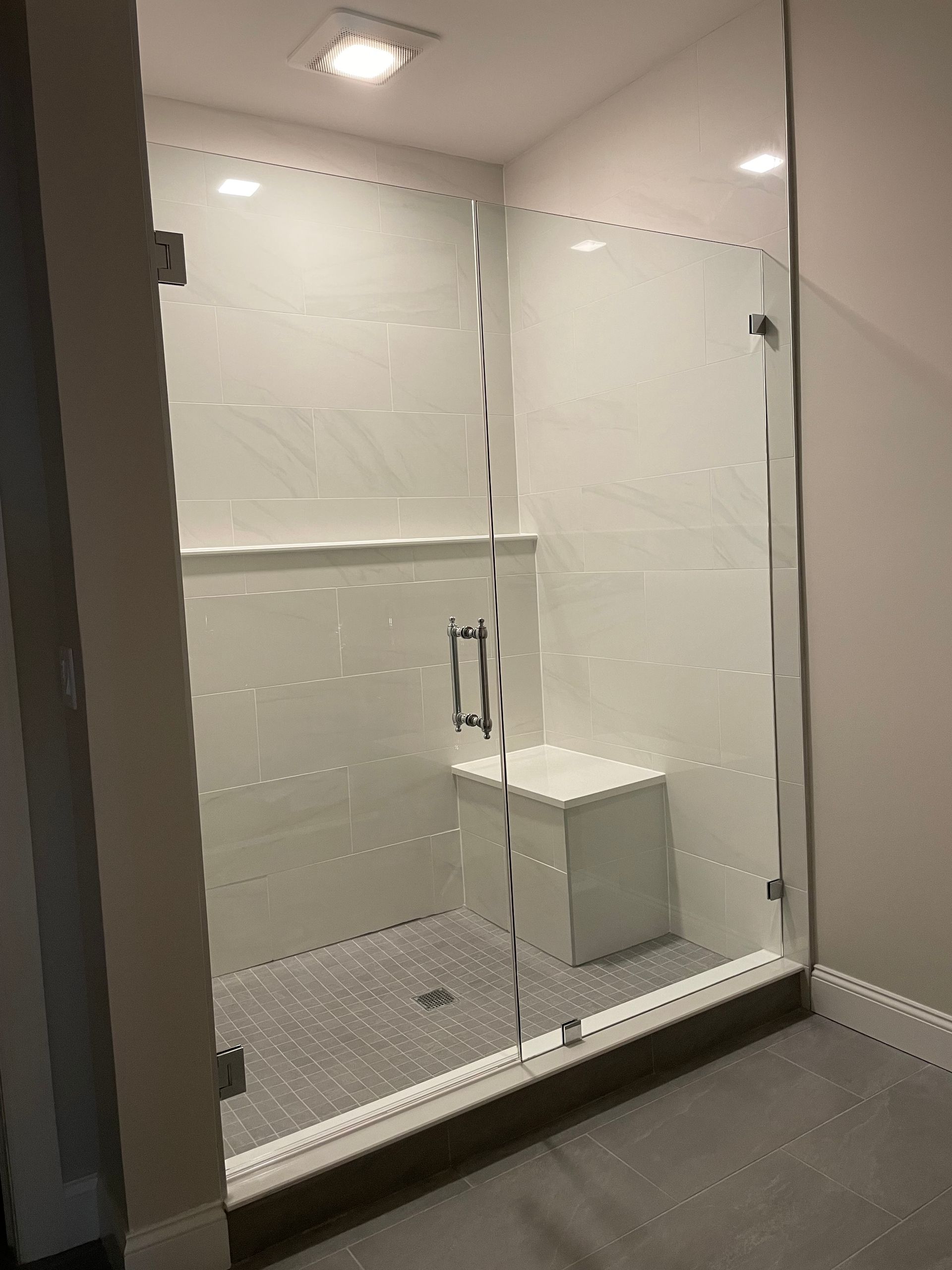 A bathroom with a glass shower door and a bench.