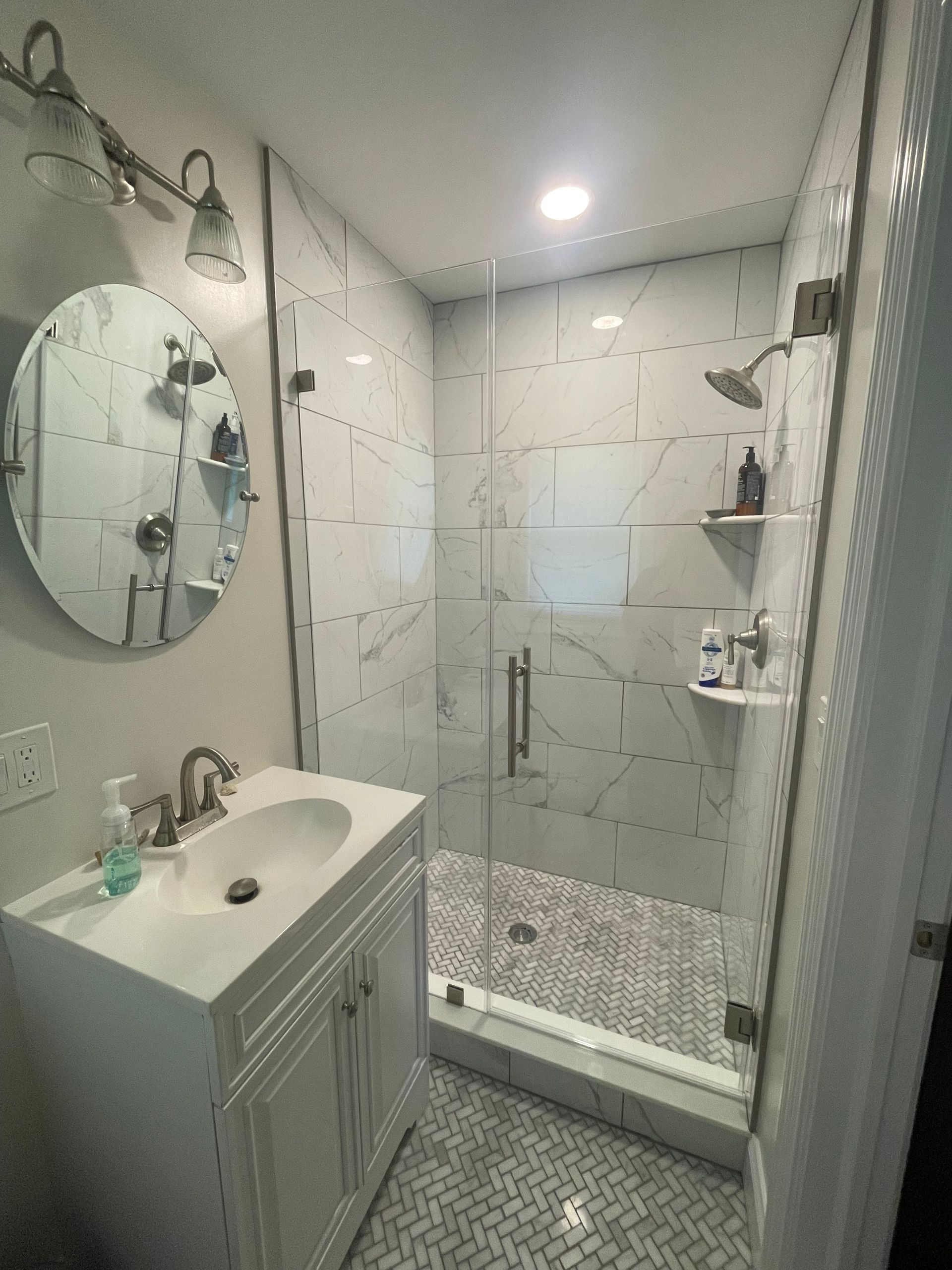 A bathroom with a sink , mirror and walk in shower.