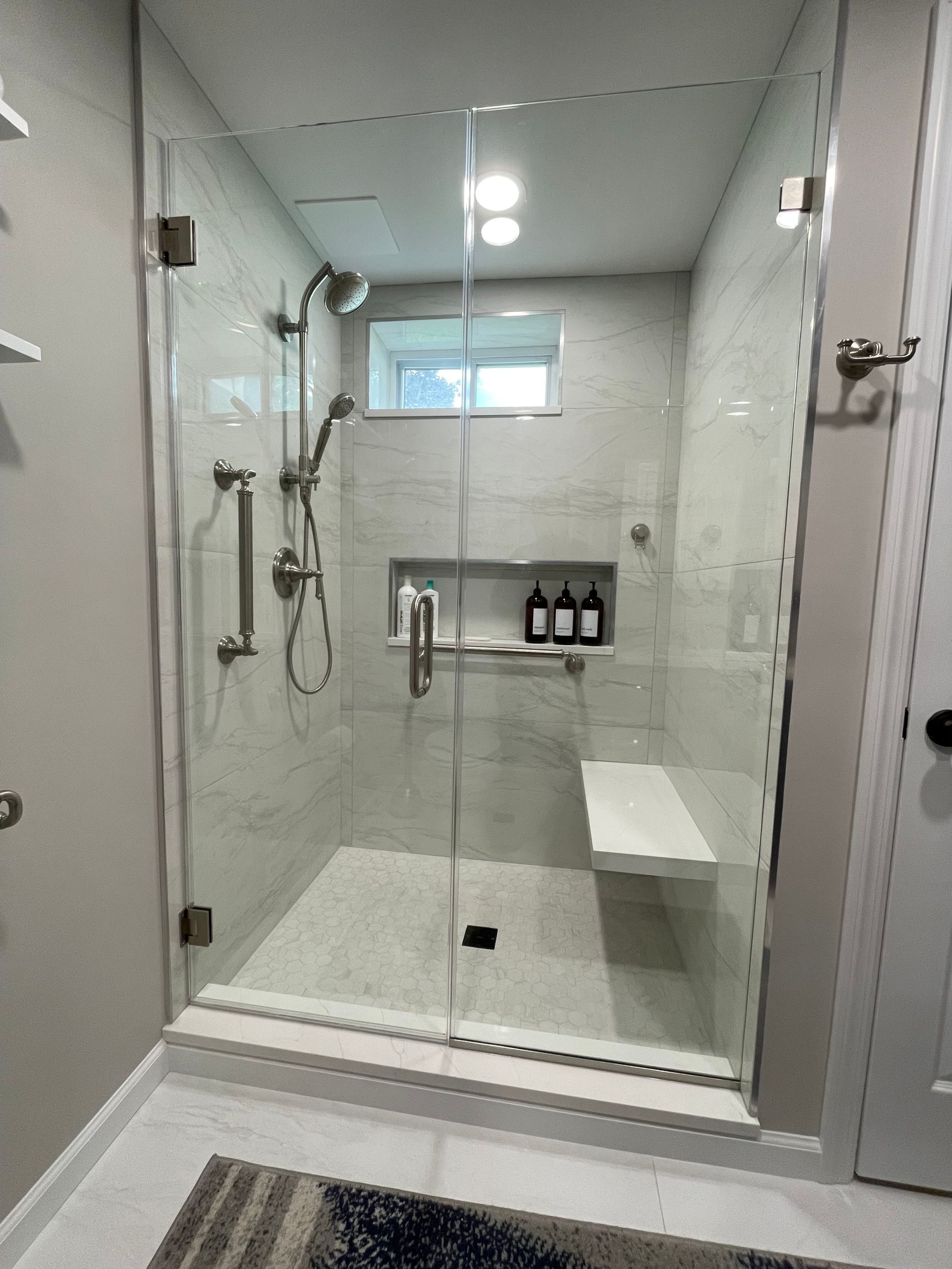 A bathroom with a walk in shower with a glass door and a bench.
