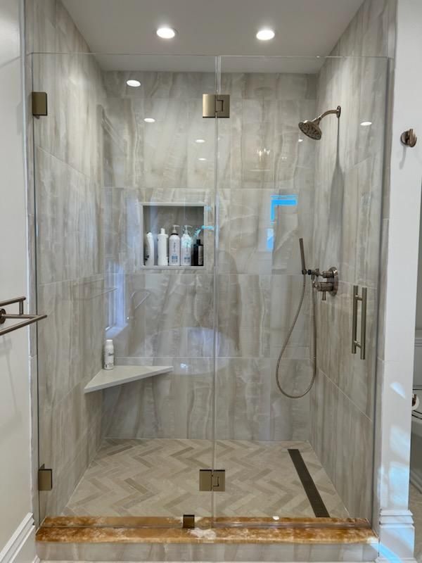 A bathroom with a walk in shower with a glass door and a bench.