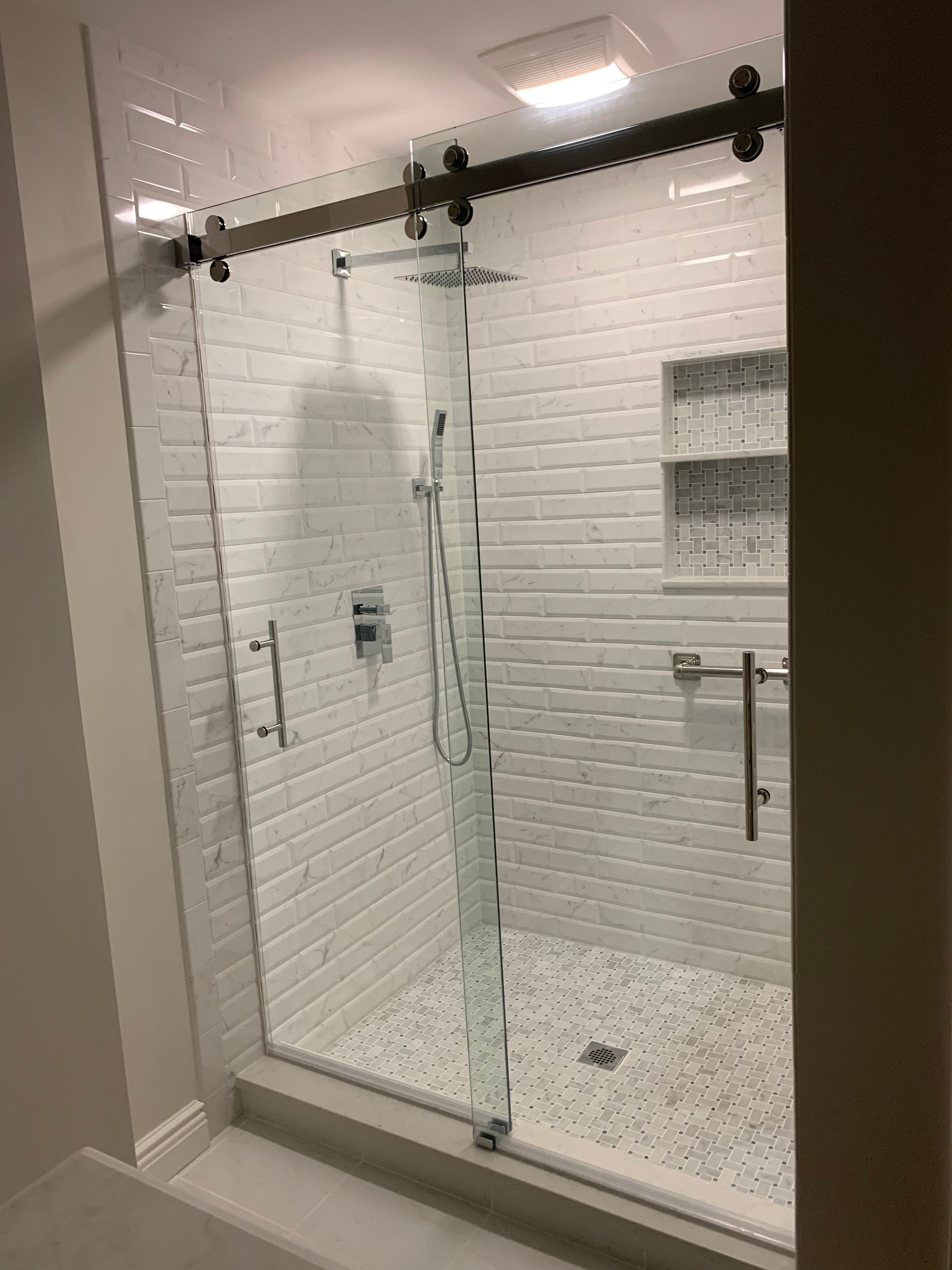 A bathroom with white tiles and a sliding glass shower door.