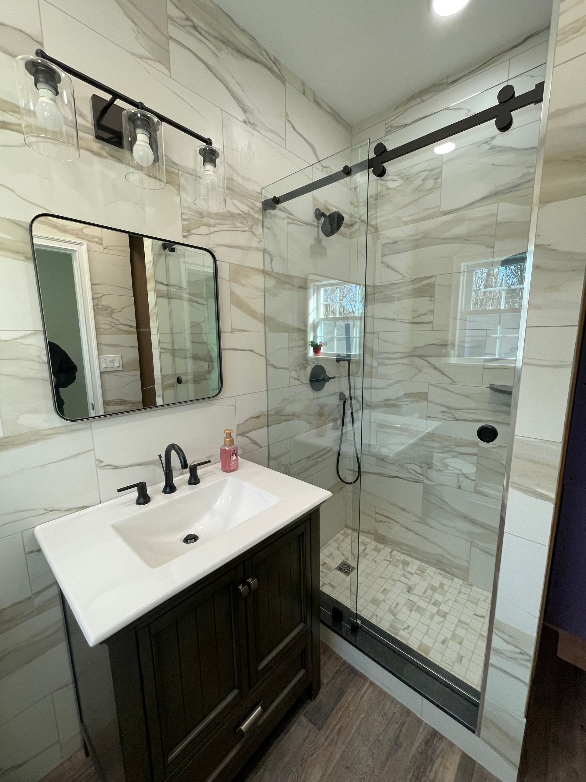 A bathroom with a sink , mirror , and sliding glass shower door.