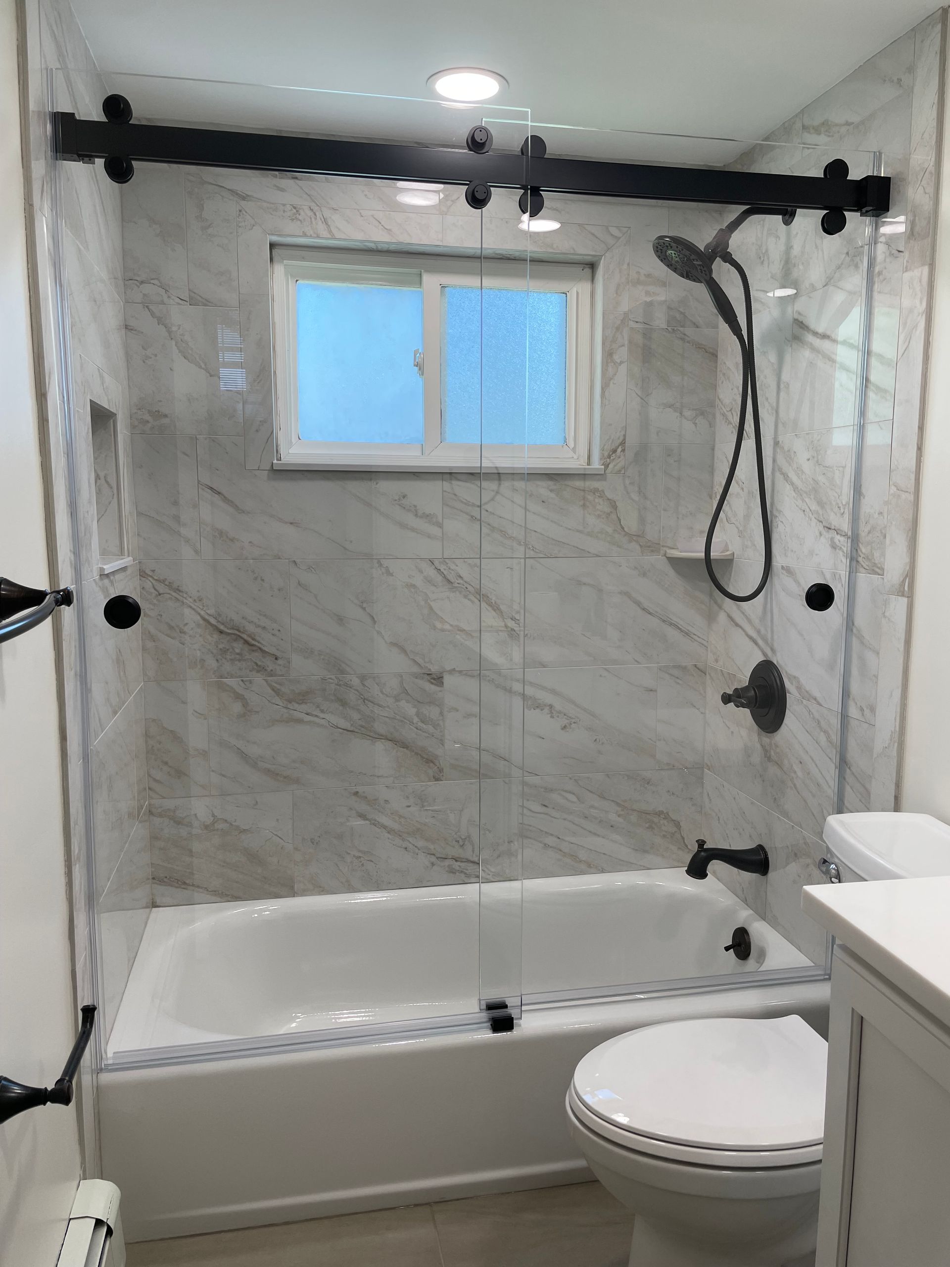 A bathroom with a tub , toilet , shower and window.