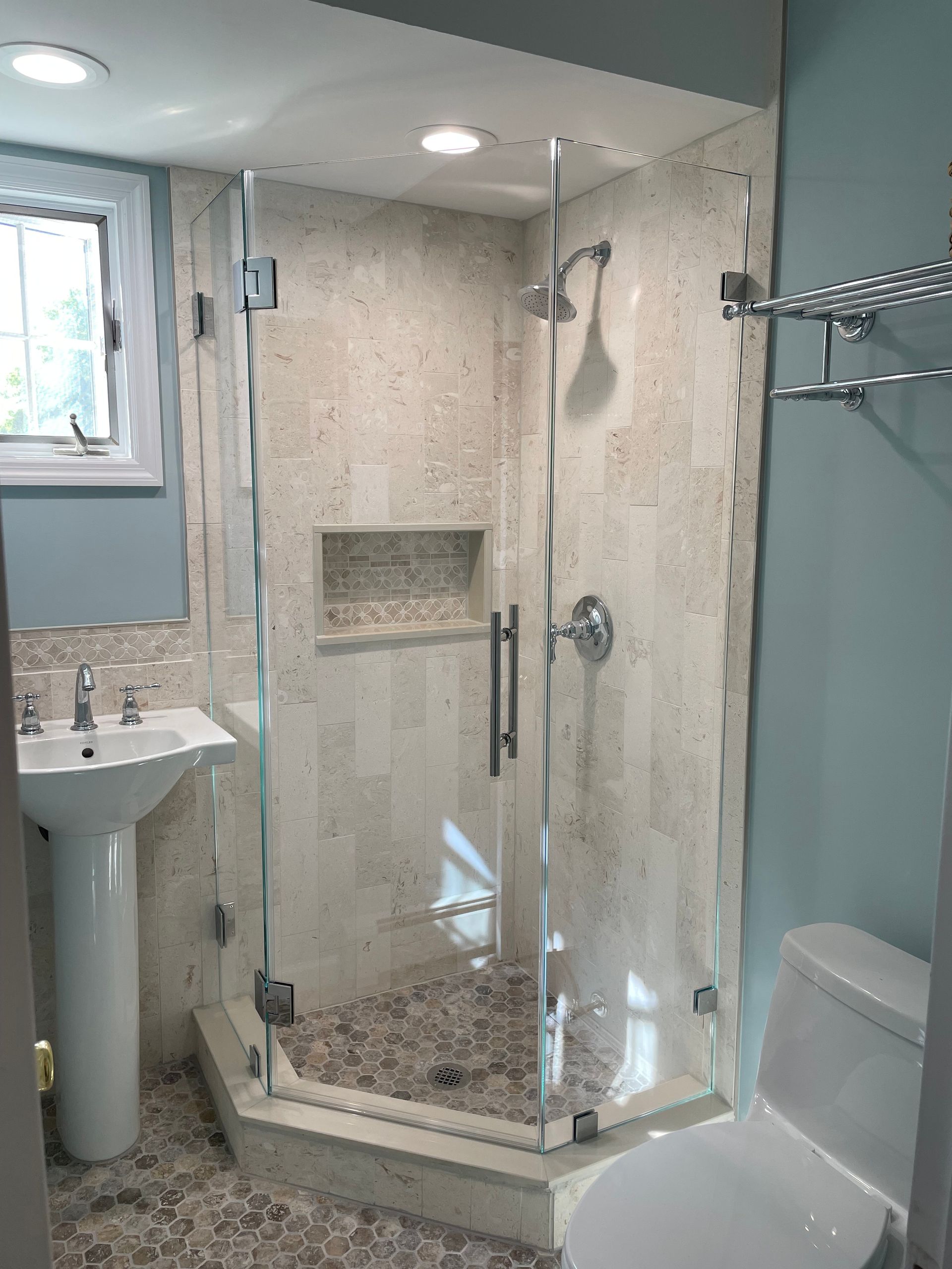 A bathroom with a shower , toilet , sink and window.