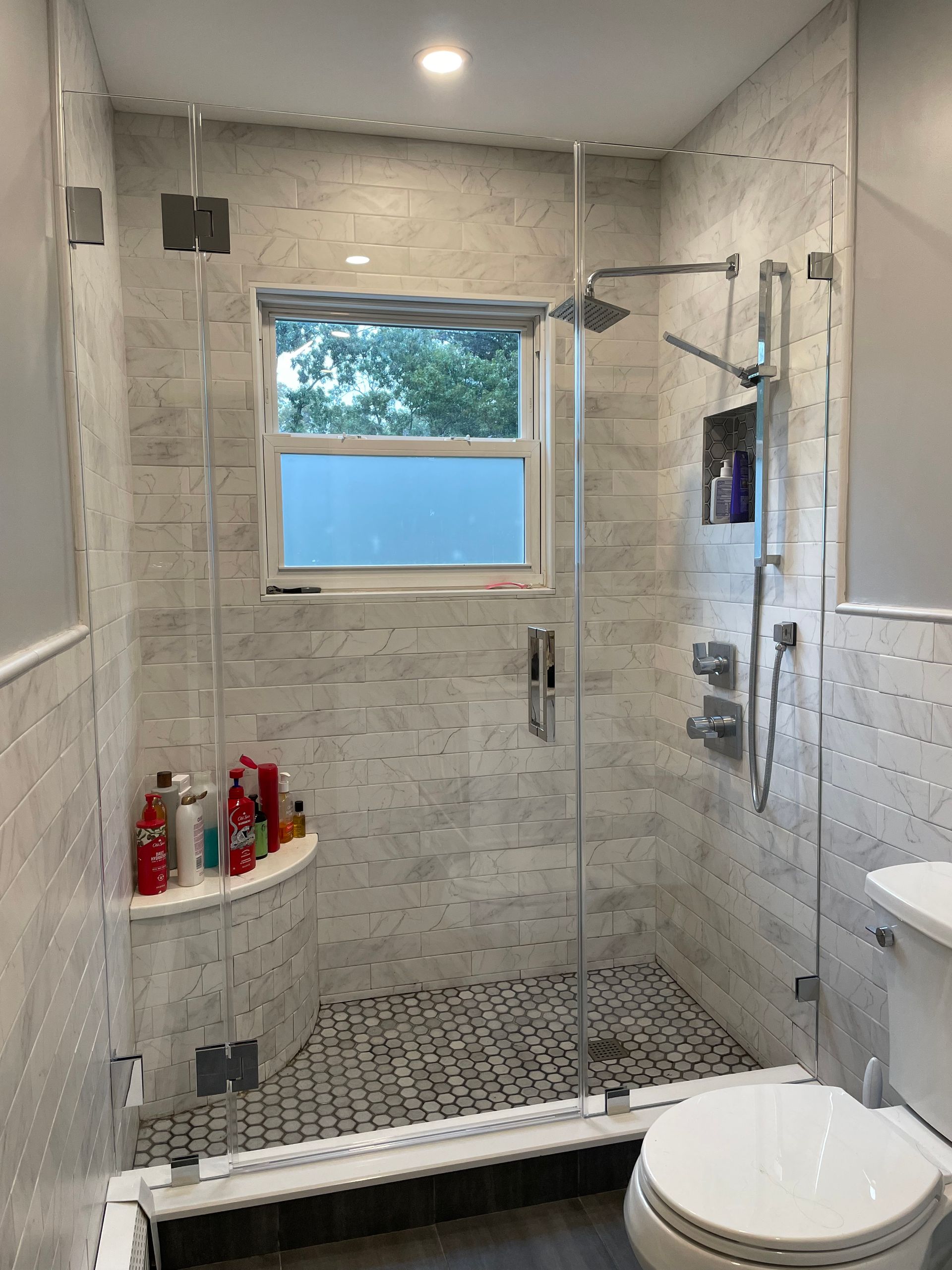 A bathroom with a walk in shower , toilet and window.