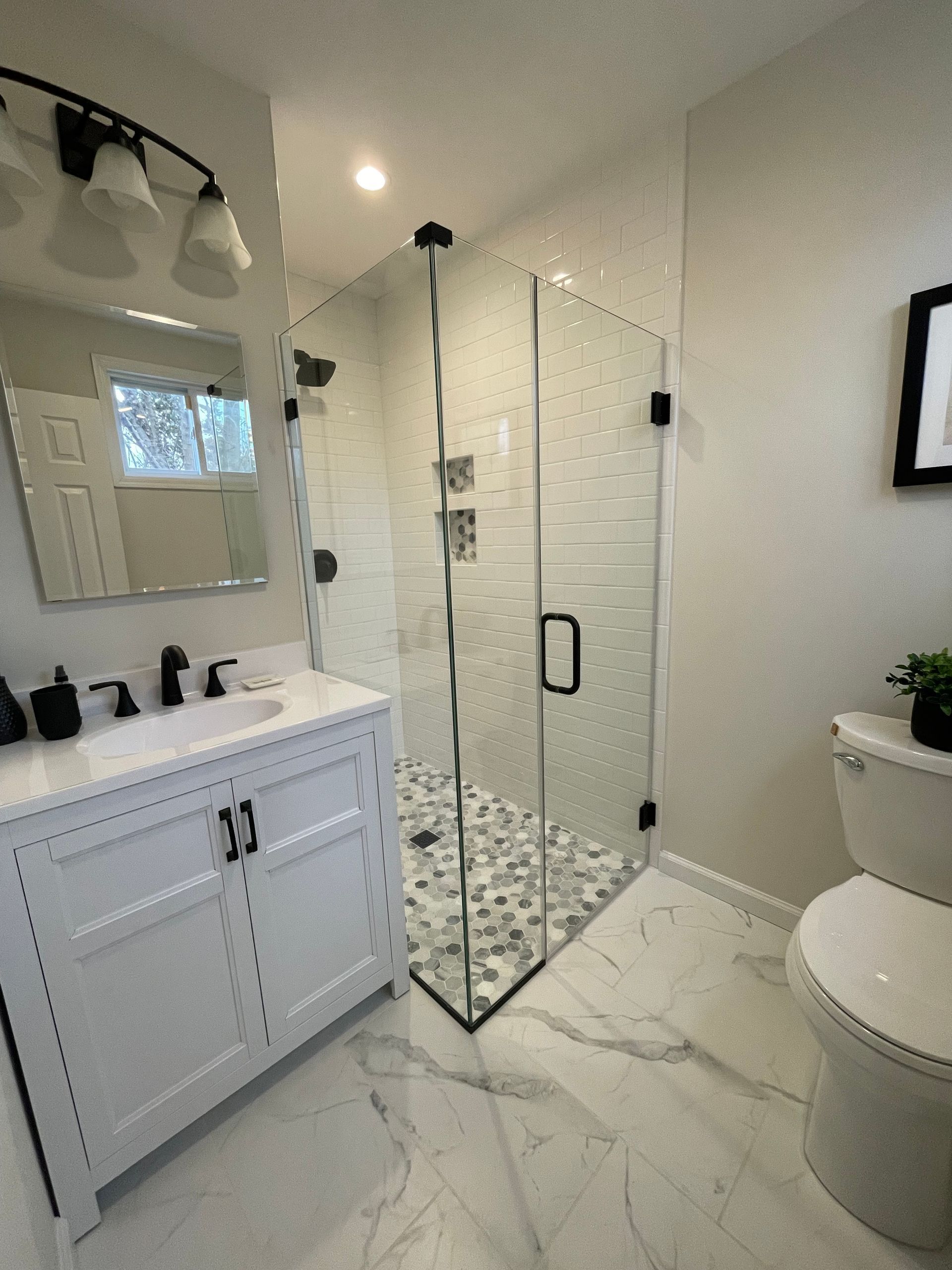 A bathroom with a toilet , sink , mirror and walk in shower.
