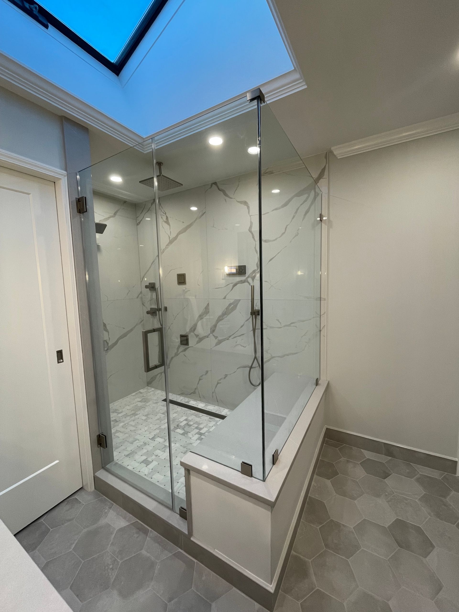 A bathroom with a walk in shower with a skylight above it.