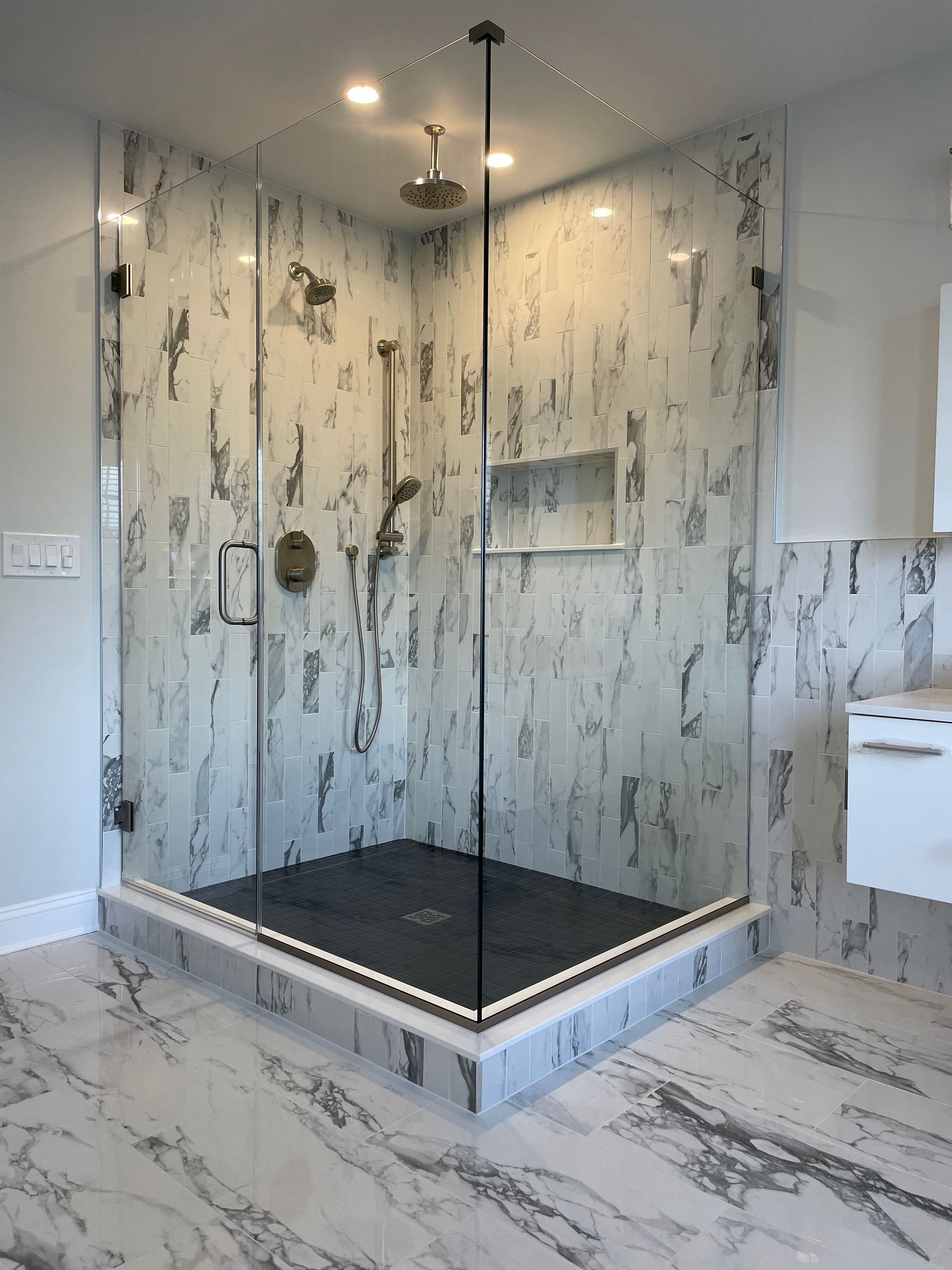 A bathroom with marble tiles and a walk in shower with a glass door.
