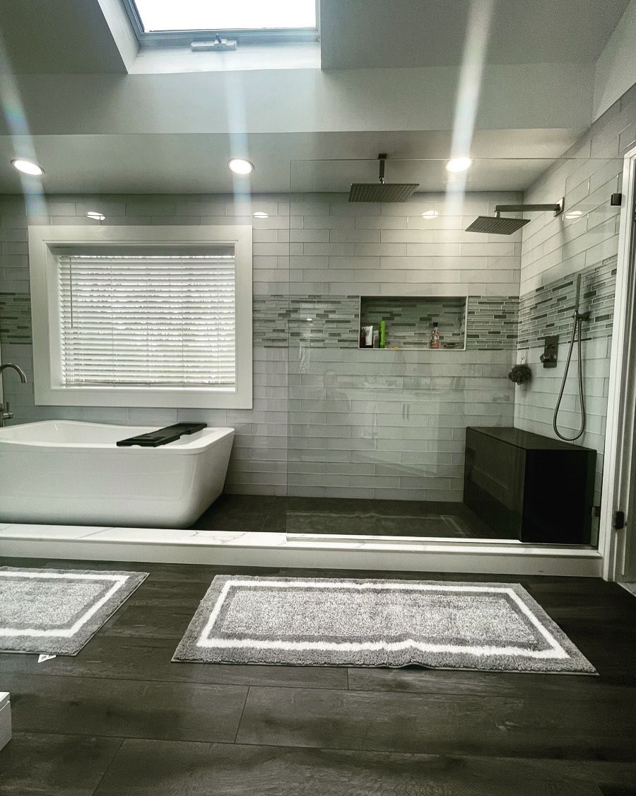 A bathroom with a tub , shower , window and skylight.