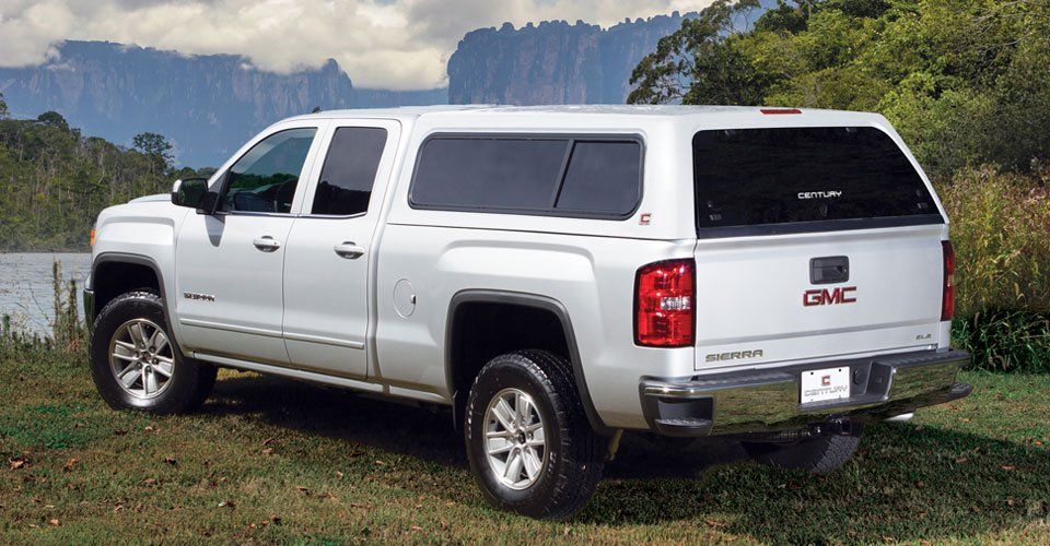 A white gmc truck is parked in the grass near a lake.
