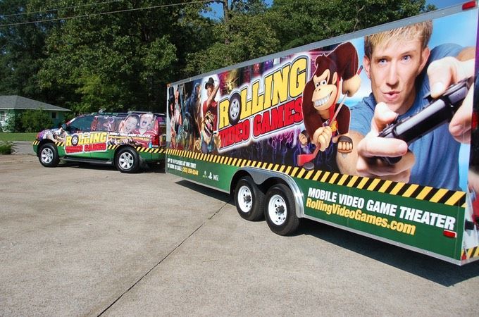 Vehicle and trailer for Rolling Video Games, with colorful graphics of video game characters, parked outdoors.