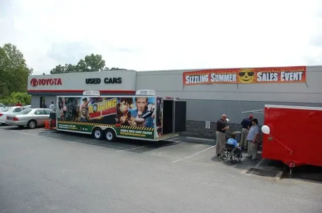 Toyota dealership with a "Skyline Summer Sales Event" banner, a trailer, and people gathering.