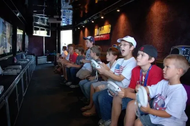 Children playing video games inside a mobile gaming truck; excited expressions, holding controllers, black interior.