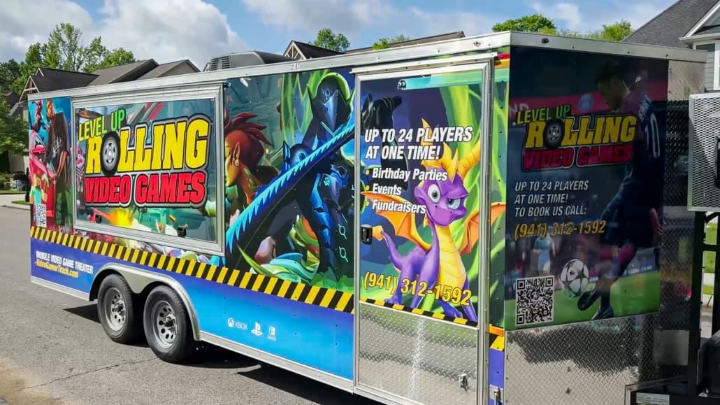 Rolling Video Games trailer with colorful game character art. Blue, yellow, and black accents, parked on a street.