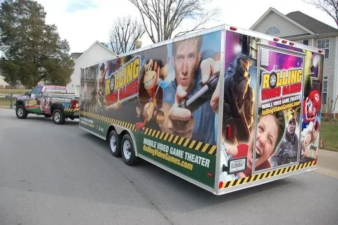 Mobile video game theater trailer with graphics and a pickup truck parked on a street.