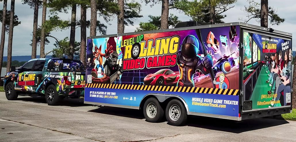 Colorfully wrapped food trailer parked beside a matching truck on a paved lot near trees
