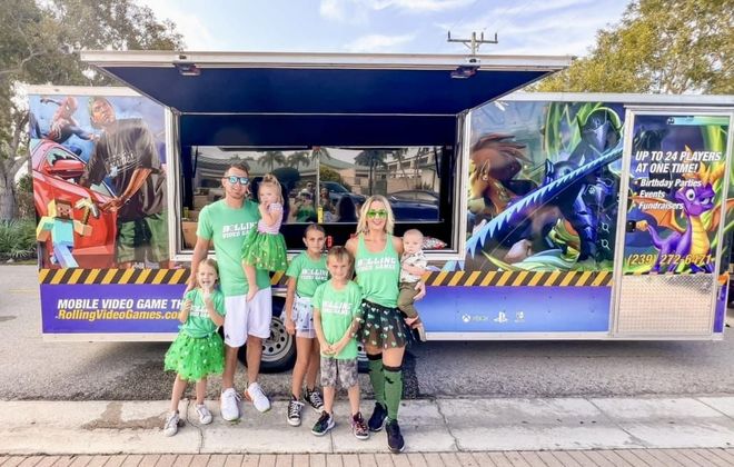 Family in green shirts and accessories poses in front of a game truck with character art.