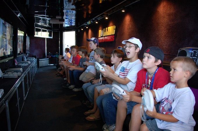 Children playing video games inside a gaming truck. Excited expressions, controllers in hand, black interior.