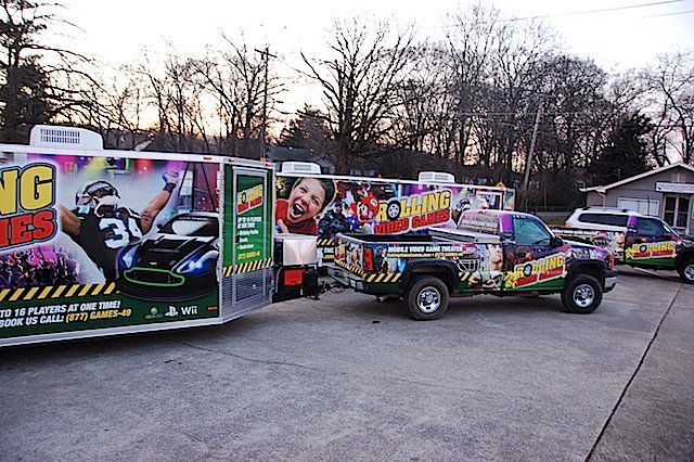 Trucks and trailers with gaming-themed graphics parked outside. Evening setting, some tree coverage.