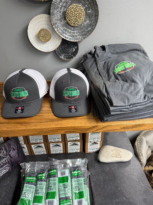Gray hats, folded shirts, and packaged items with green logos arranged on a wooden table.