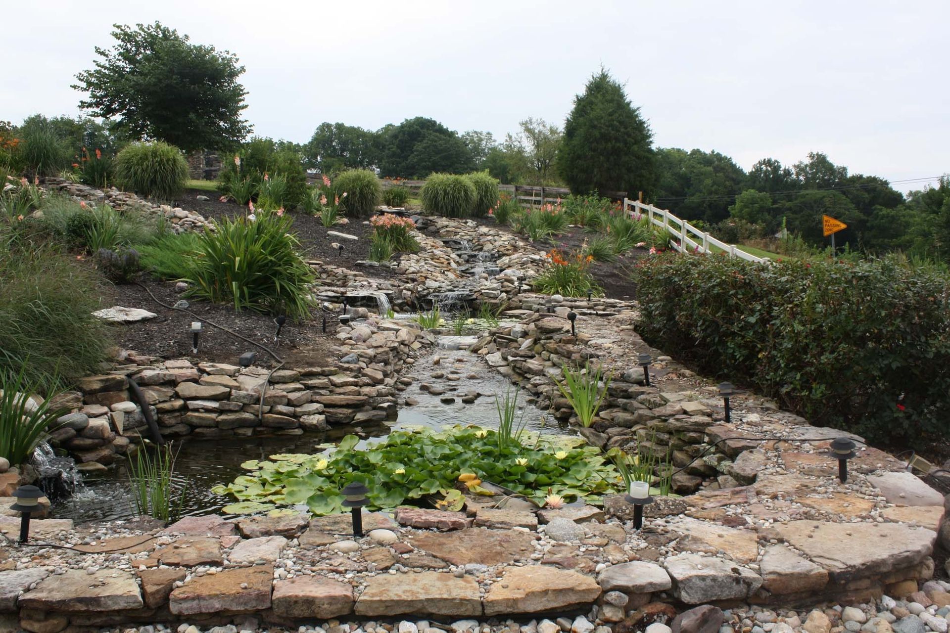 Rock garden with stacked stone terraces, shrubs, and a small stream in a landscaped park