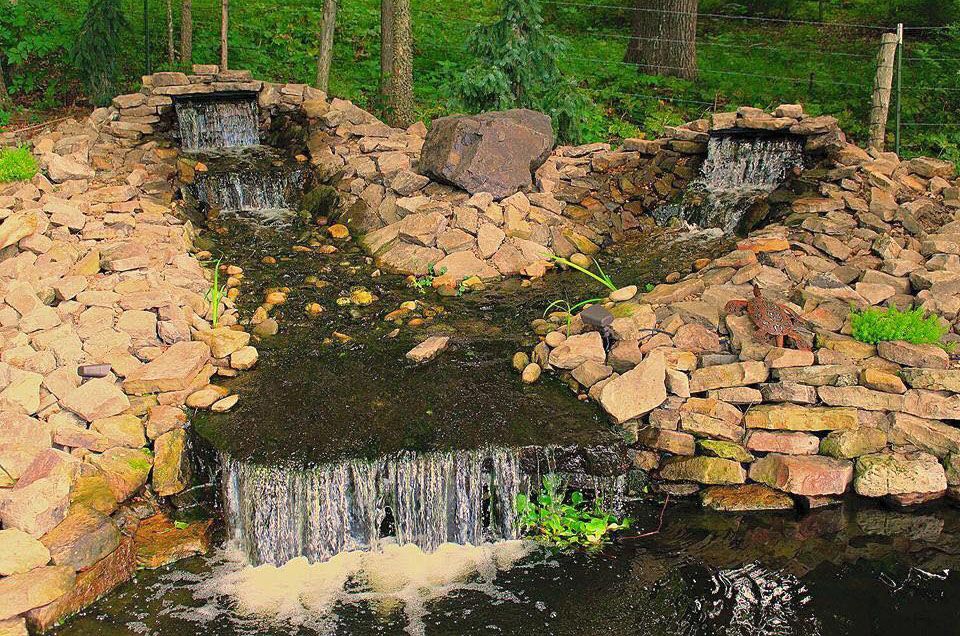 Stone-lined stream with a small waterfall and green trees in the background