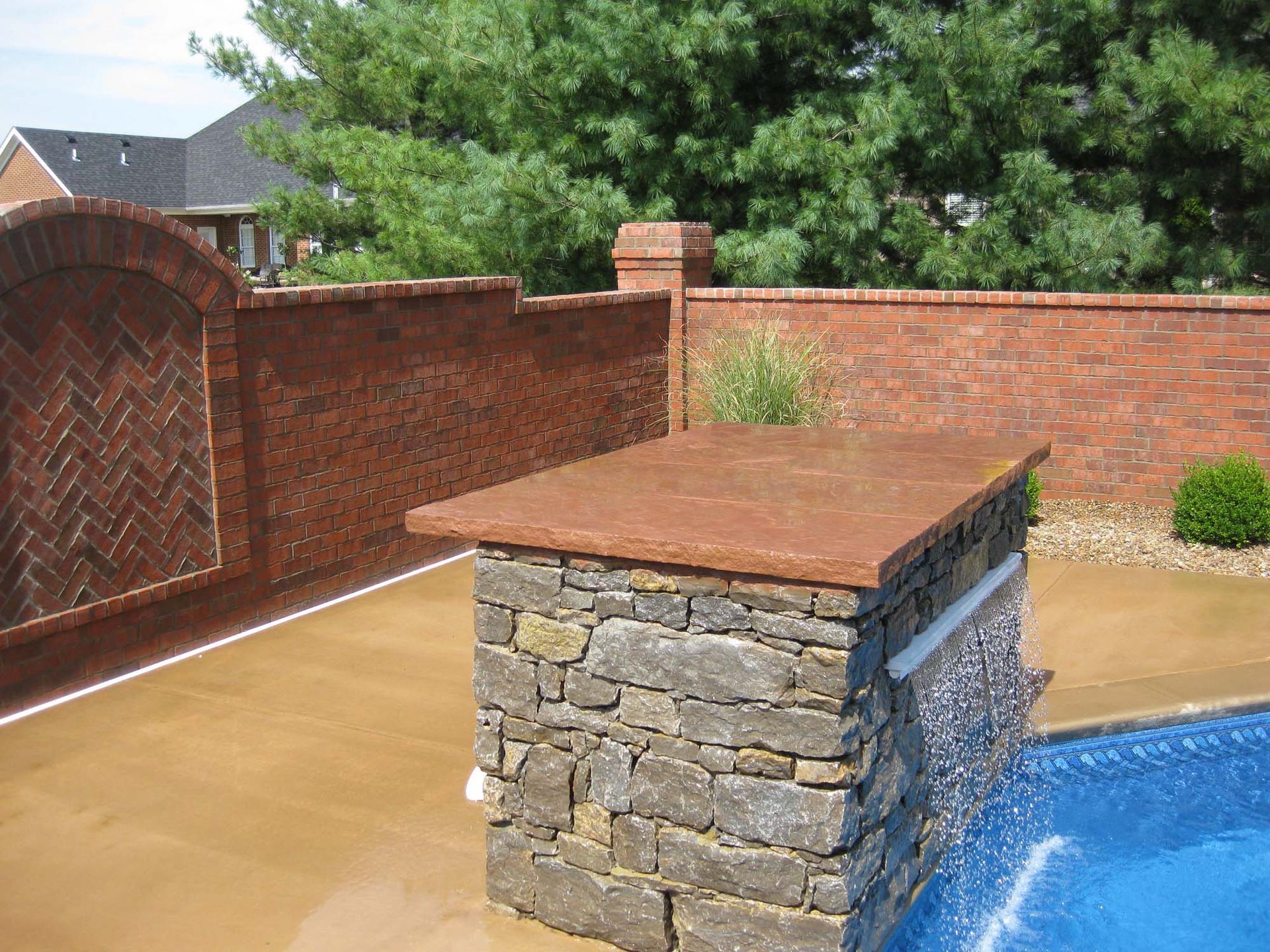 Stone outdoor grill or planter with a copper top on a brick patio beside a red brick wall and trees