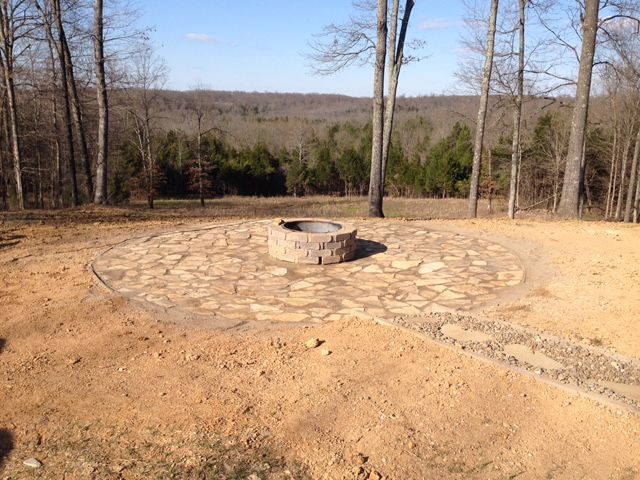 Stone fire pit in a cleared yard overlooking a wooded landscape