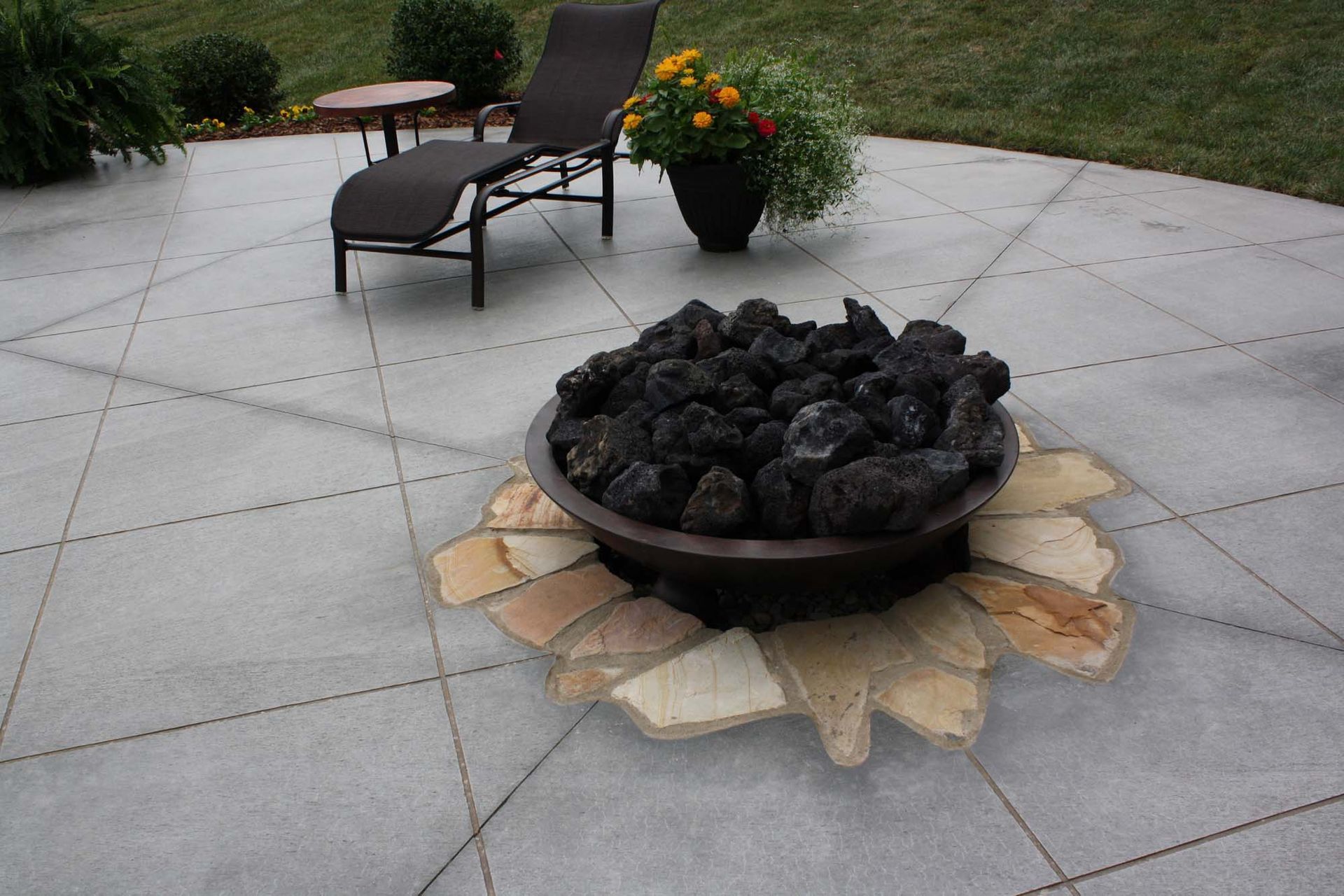 Patio fire pit filled with lava rocks on a stone patio, with chairs and potted plants nearby