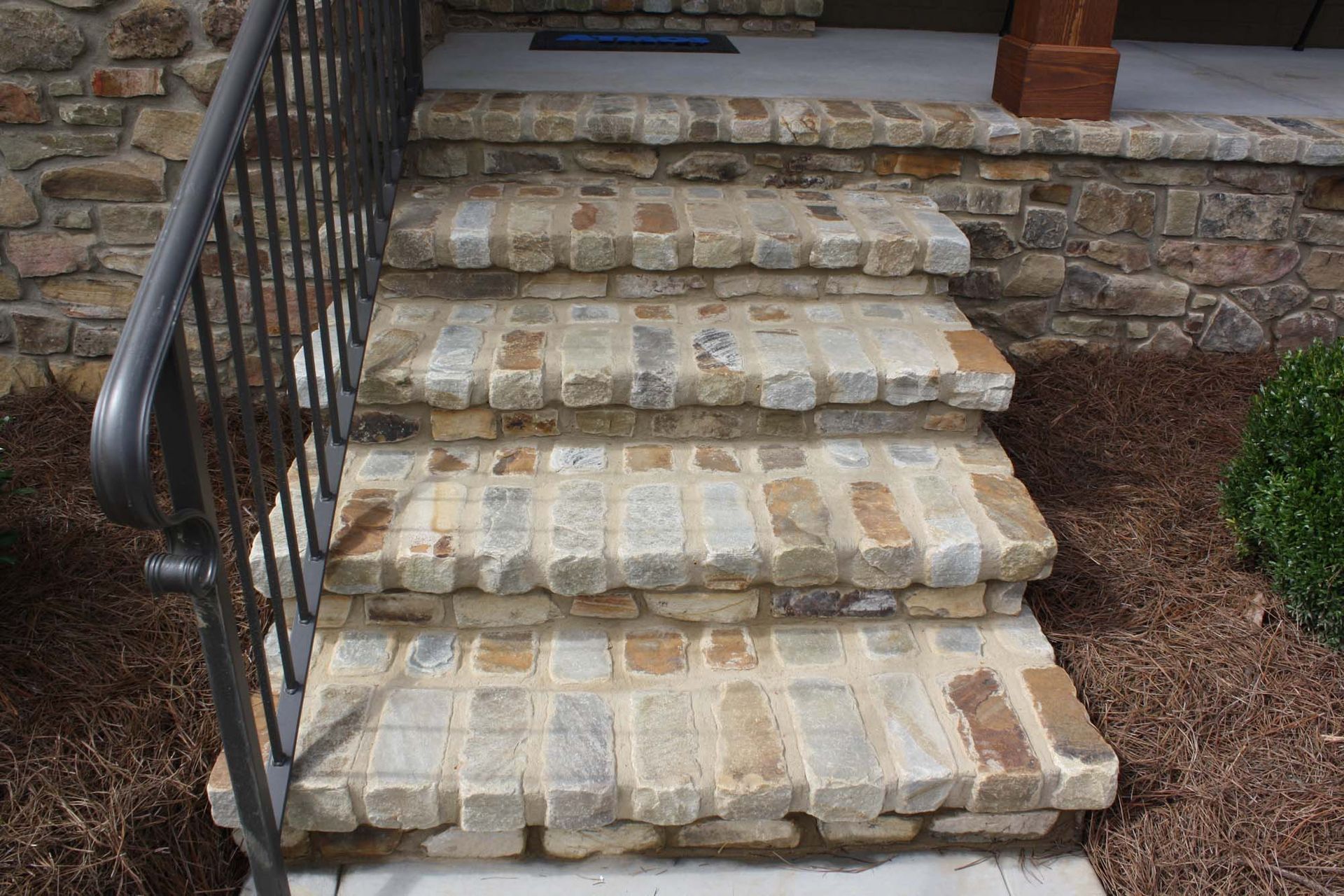 Stone front steps with a black handrail leading to a house entrance