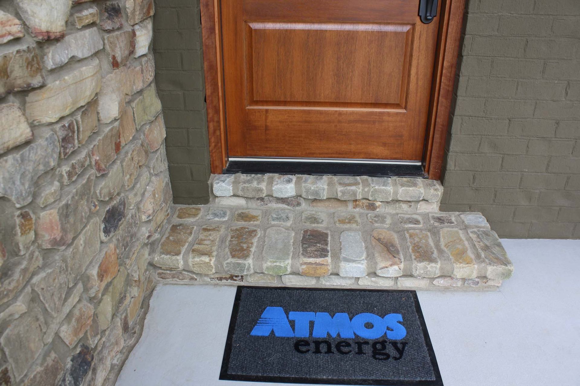 Front door with stone step and black Atmos Energy doormat at the entrance
