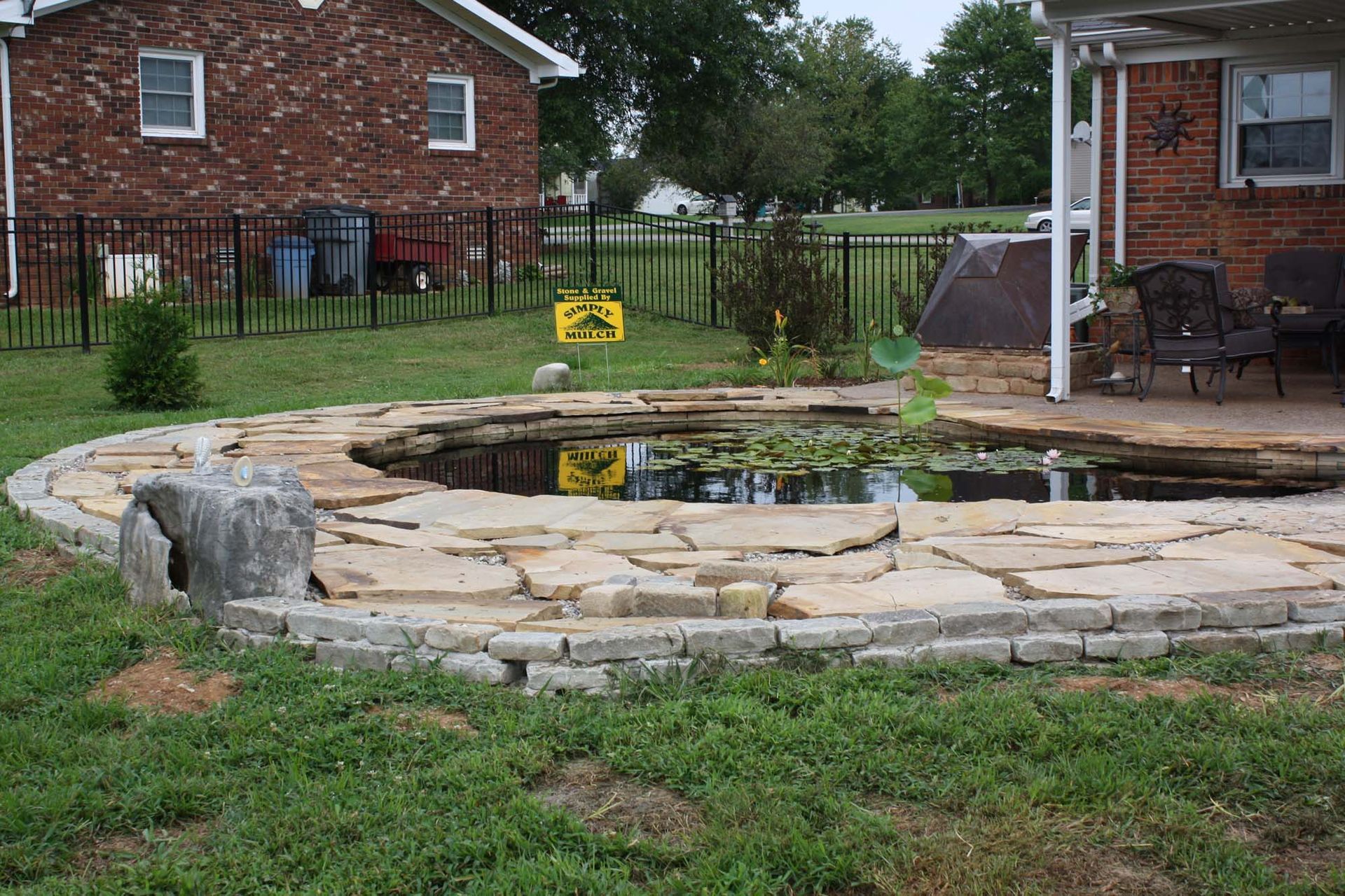 Backyard stone pond with water, rocks, and brick houses in the background