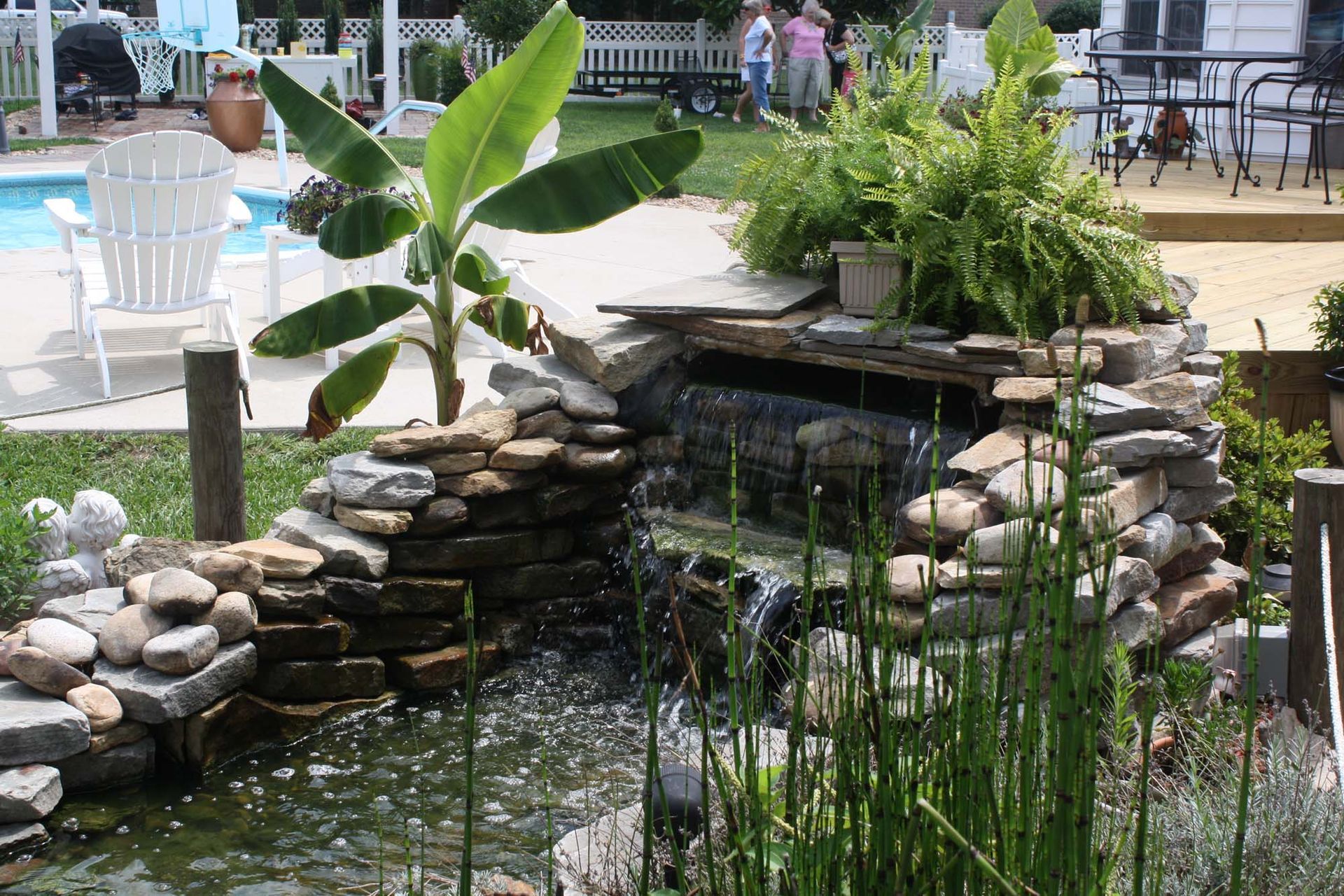 Stone pond waterfall in a garden with green plants and a banana tree