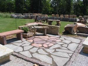 Stone patio with benches and a built-in stone fire pit in a grassy outdoor area