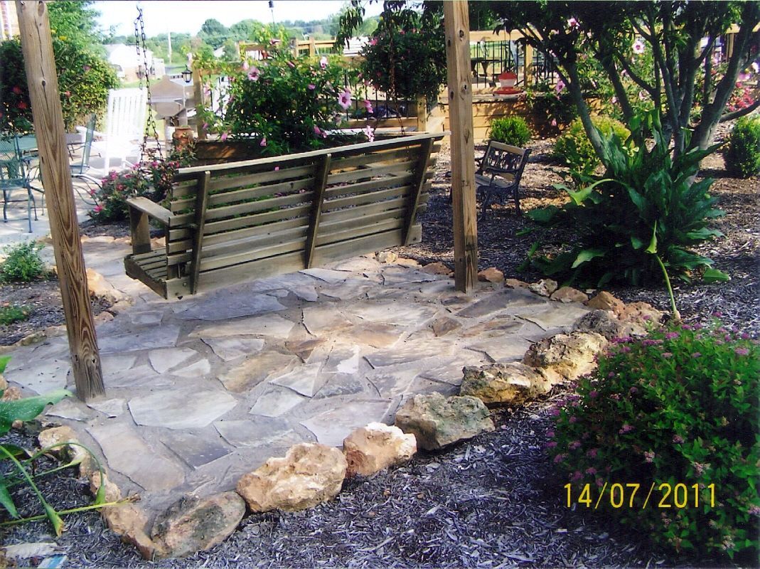 Stone garden path with a wooden bench under trees and flowering shrubs