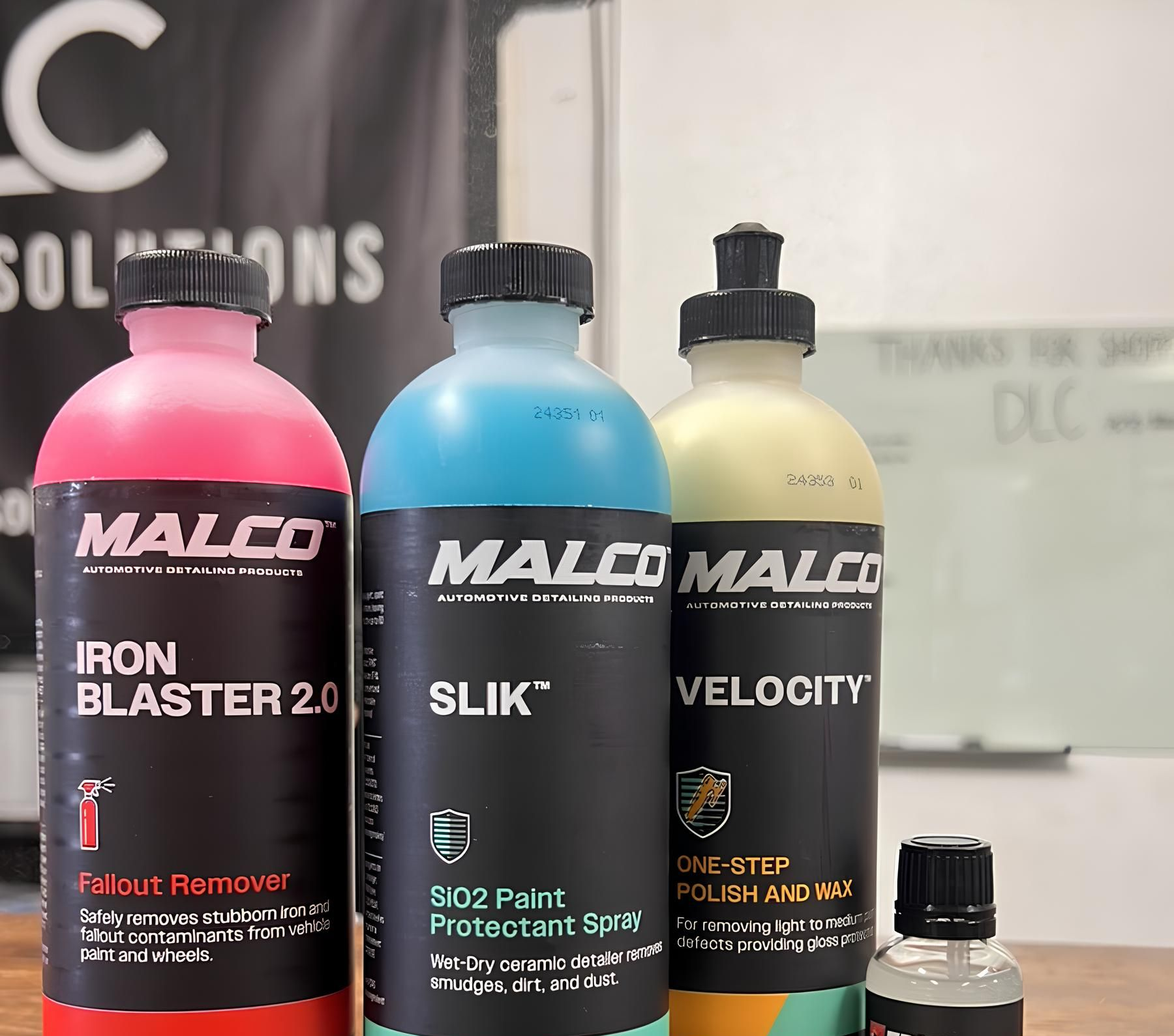 Three bottles of Malco car care products: Iron Blaster, SLIK, and Velocity, with a small bottle in front.