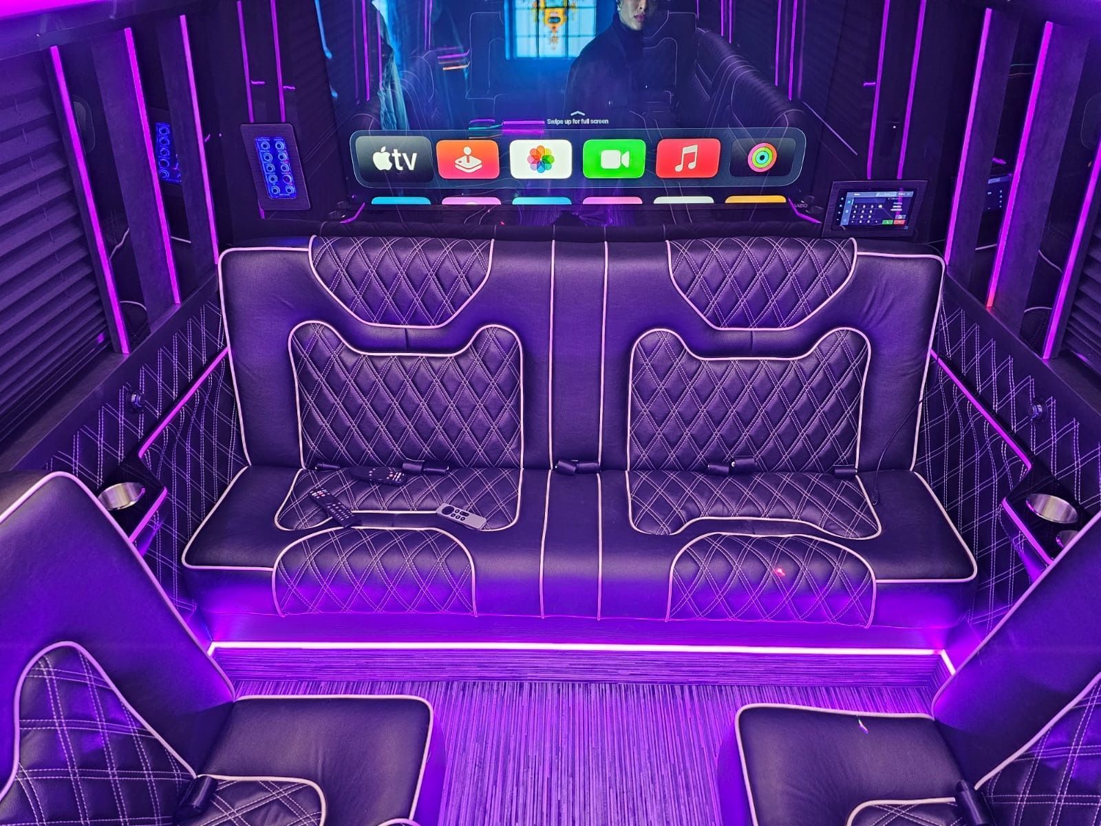 Purple-lit luxury van interior with quilted seats and a TV screen above the front partition