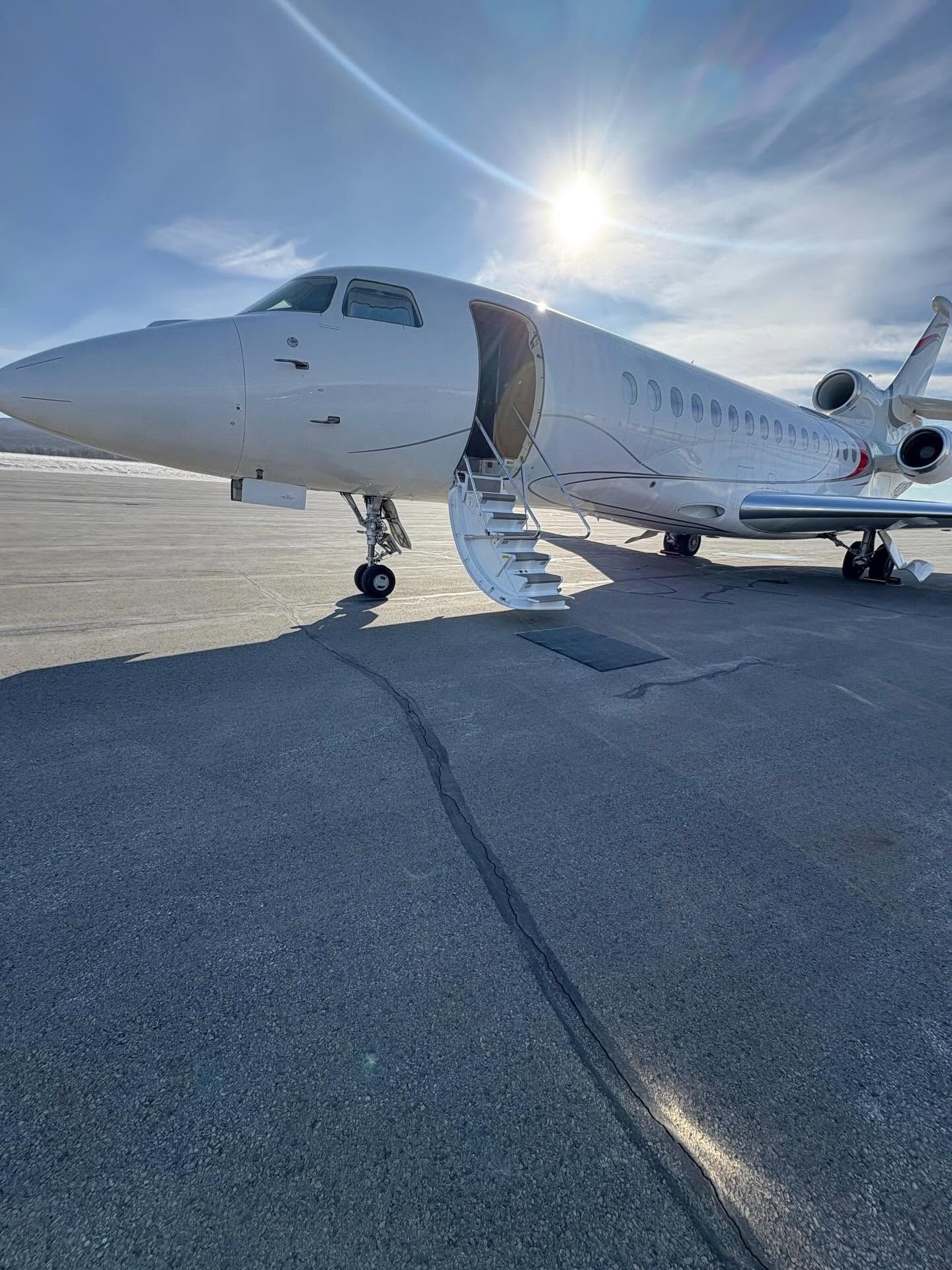 Private jet on tarmac with stairs lowered, sun shining overhead.