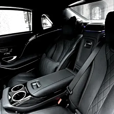 Black luxury car back seat with quilted leather, center armrest, and cup holders in a dark interior.