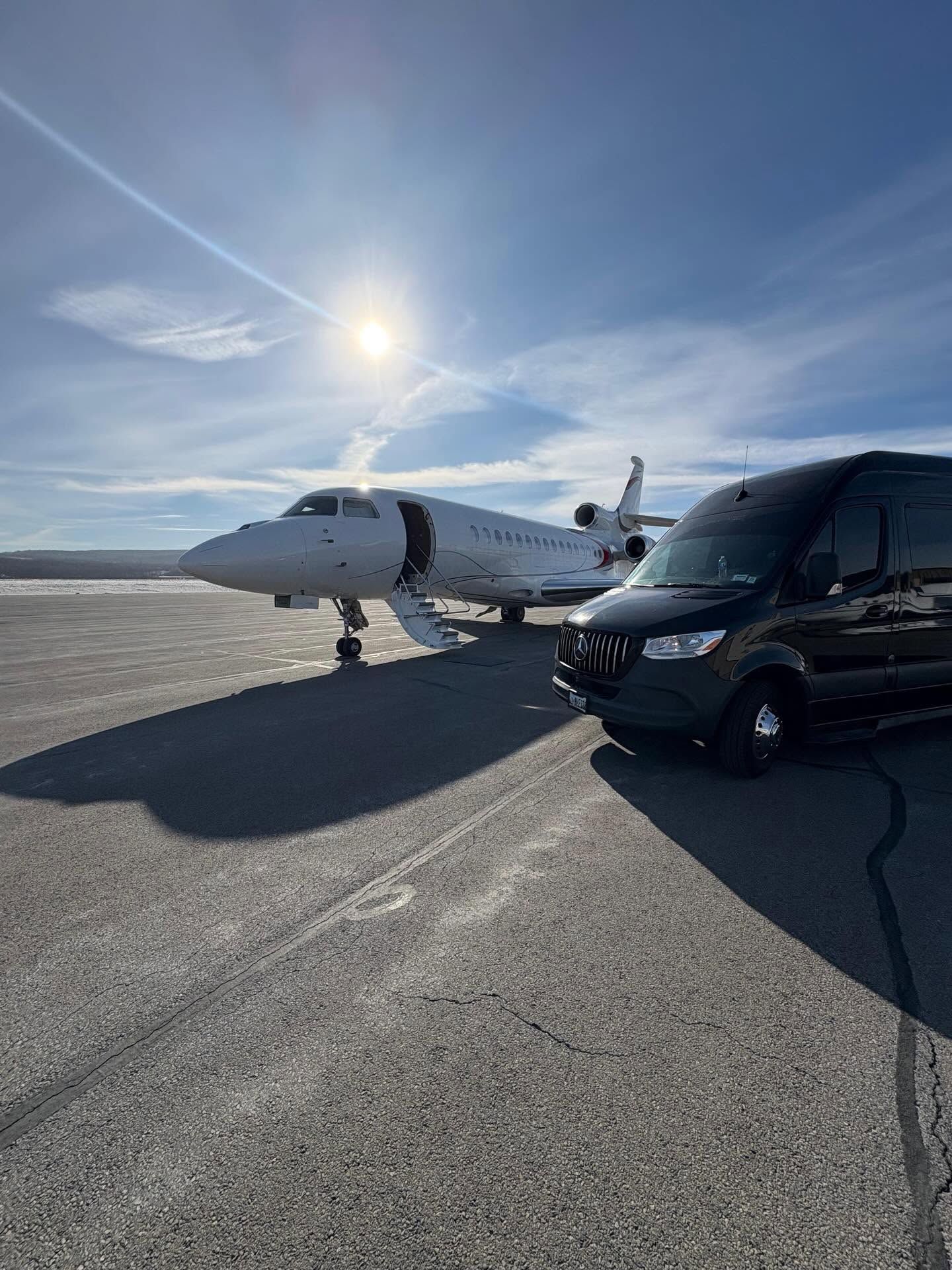 Small private jet parked on a sunny runway beside a black van under a blue sky