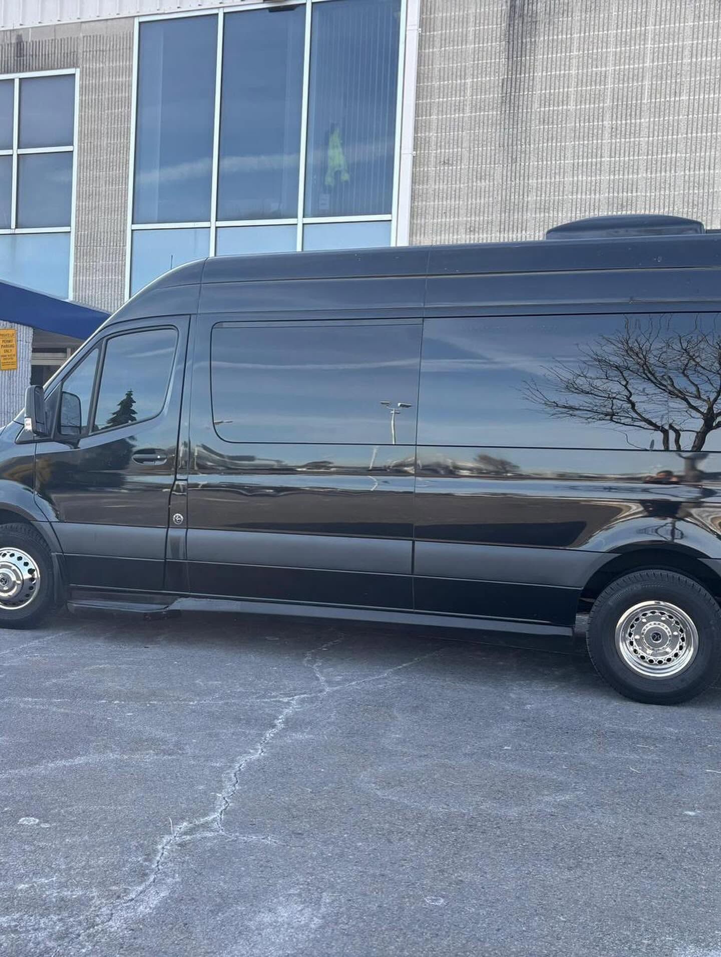 Black passenger van parked outside a building with large windows and a gray wall.