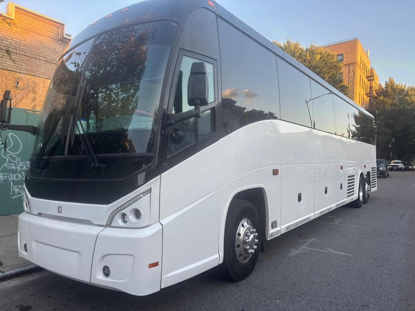 White coach bus parked on a street beside buildings at sunset.