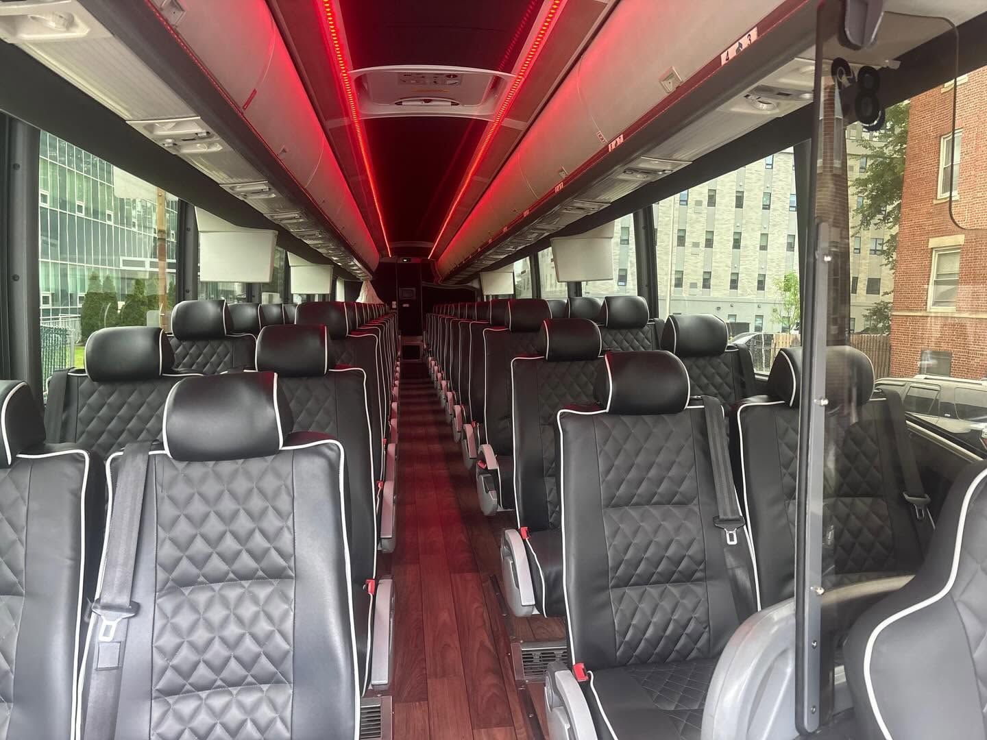 Empty luxury bus interior with black quilted seats and red ceiling lights, viewed down the aisle