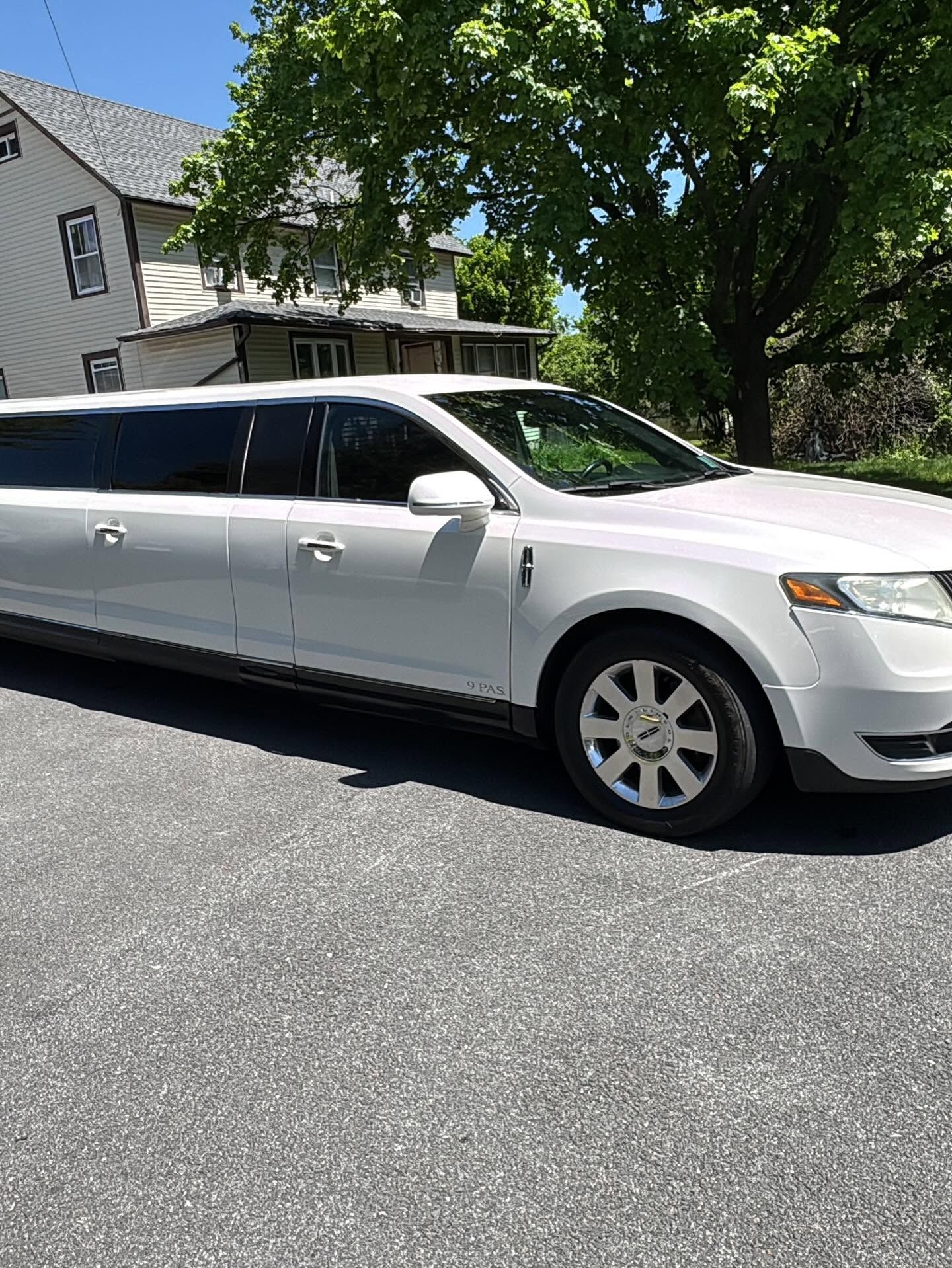 White sedan parked on a sunny residential street beside a house and trees