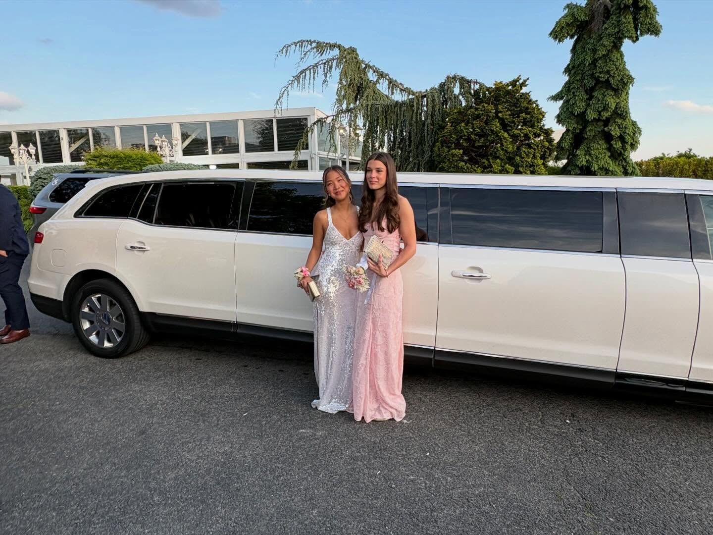 Two women posing beside a white stretch limousine outdoors at dusk