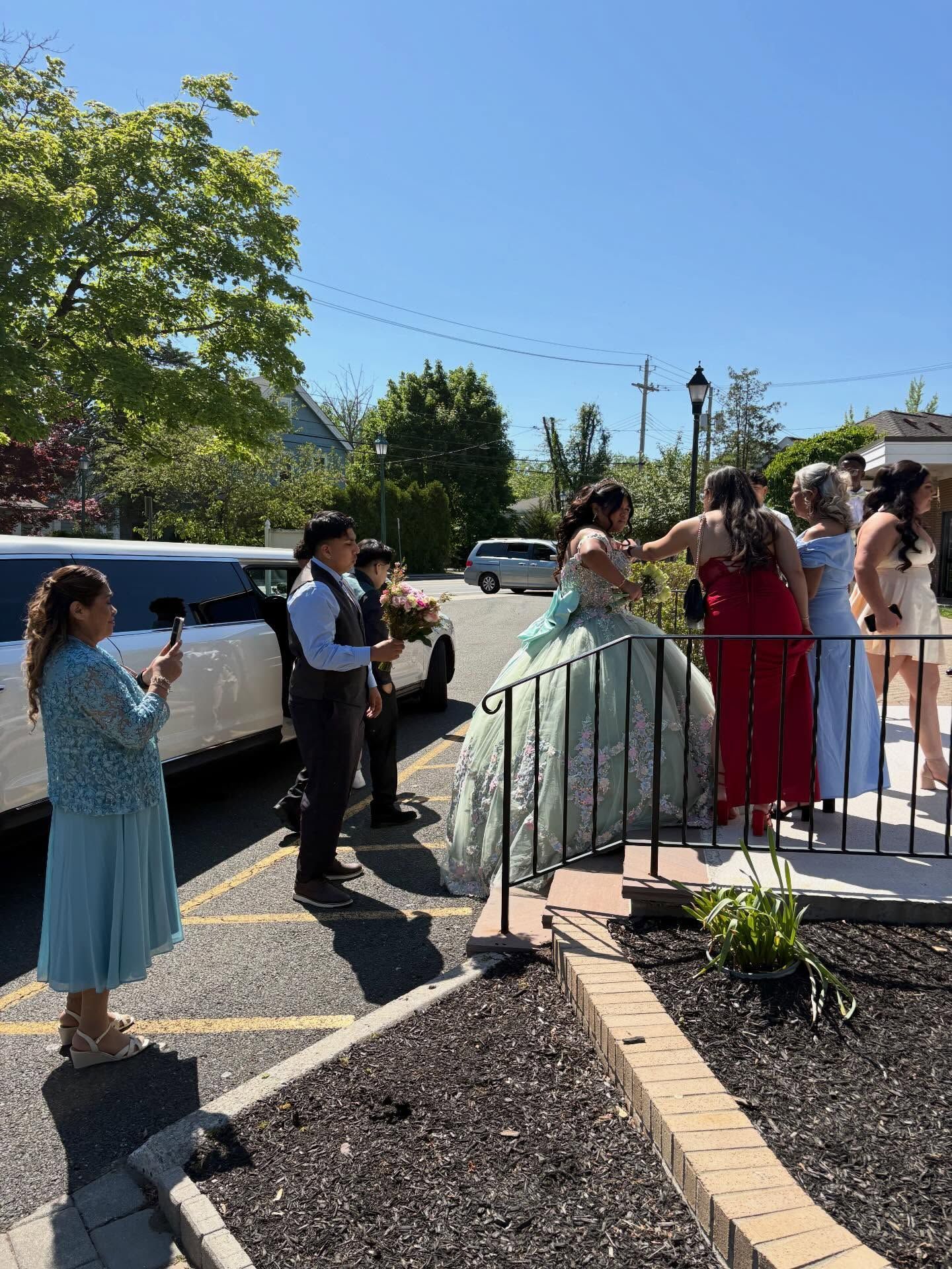 Outdoor celebration with people gathered by a white limousine near a decorated building entrance