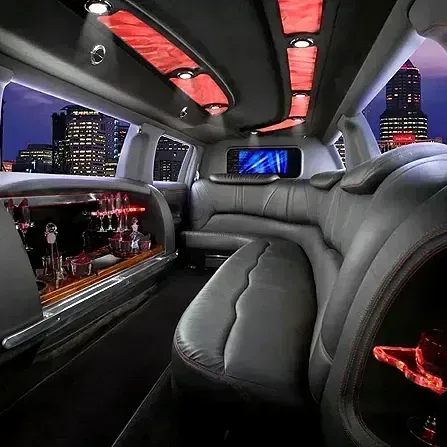 Luxury limousine interior with gray leather seats, red LED lighting, city skyline view, and a small bar.