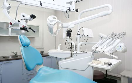 A dental office with a blue dental chair and a microscope.